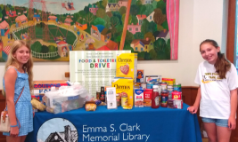 Table with Emma Clark logo on front and food items on top. Two girls flank the table.
